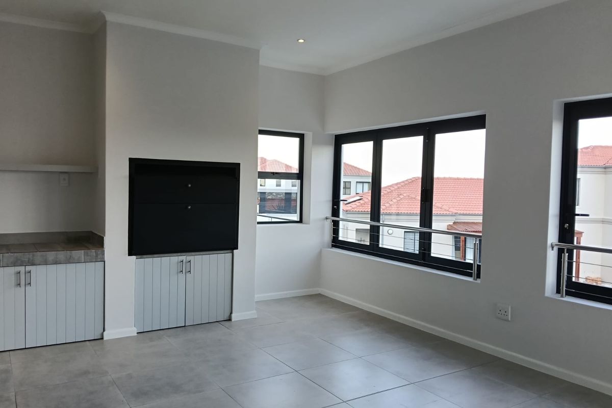 A bright, modern living area featuring large aluminium windows, tiled flooring, recessed lighting, and a built-in fireplace with integrated storage cabinetry.