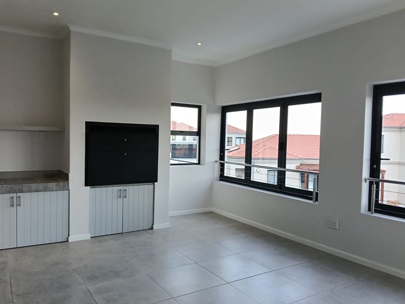 A bright, modern living area featuring large aluminium windows, tiled flooring, recessed lighting, and a built-in fireplace with integrated storage cabinetry.