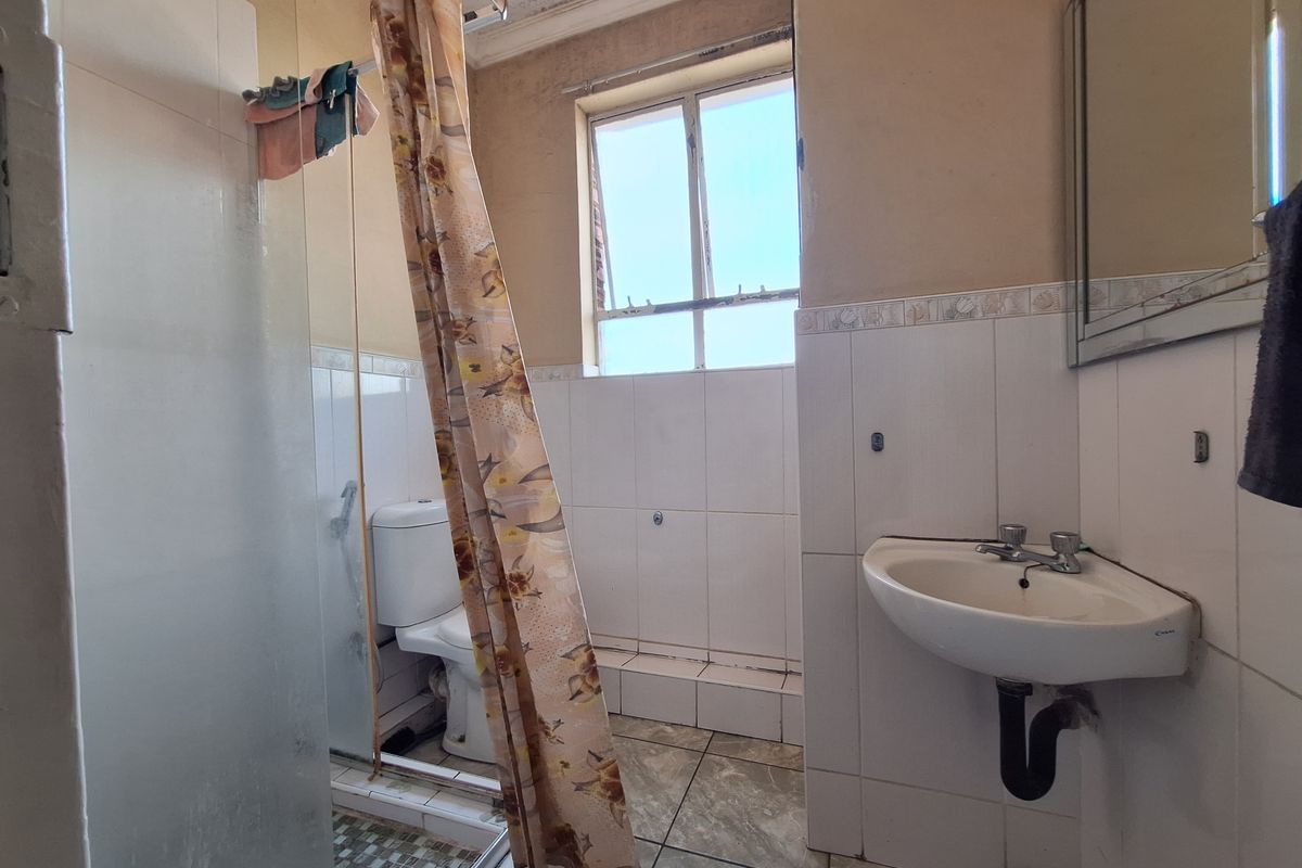 A dated bathroom featuring a shower enclosure, wall-mounted basin, and toilet, with tiled walls and flooring, requiring cosmetic updates.