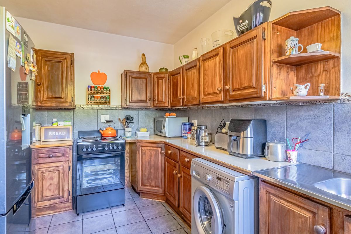 A functional kitchen featuring traditional wooden cabinetry, tiled backsplash, tiled flooring, and integrated laundry facilities, offering a practical layout for daily meal preparation.