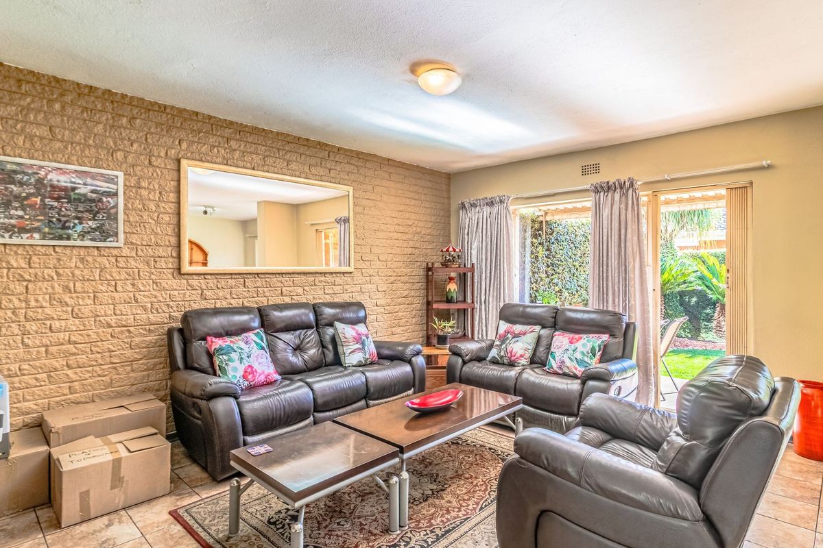 A living room featuring an exposed brick wall, tiled flooring, and a sliding glass door providing access to the garden area.