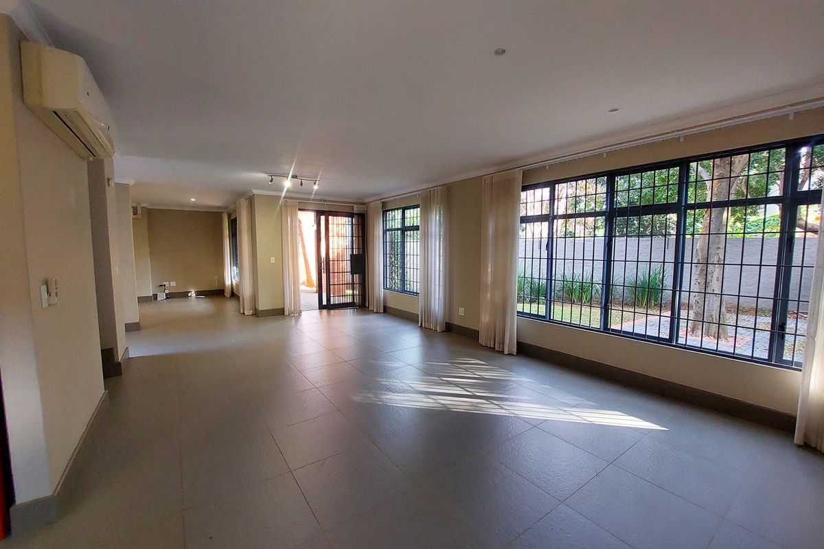 Spacious, light-filled living area featuring large windows with security bars, tiled flooring, and a wall-mounted air conditioning unit.