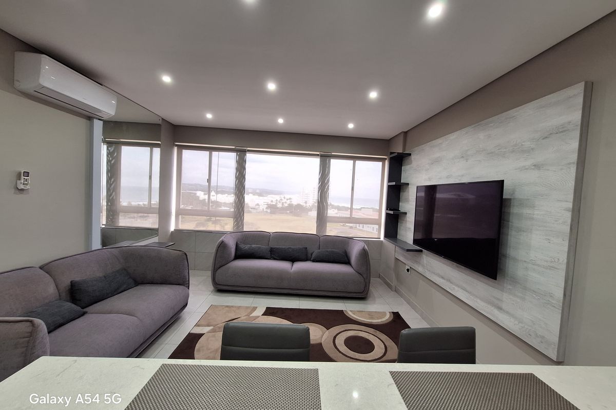 Modern living room featuring a built-in media wall, recessed downlighting, split-system air conditioning, and large windows with coastal views.