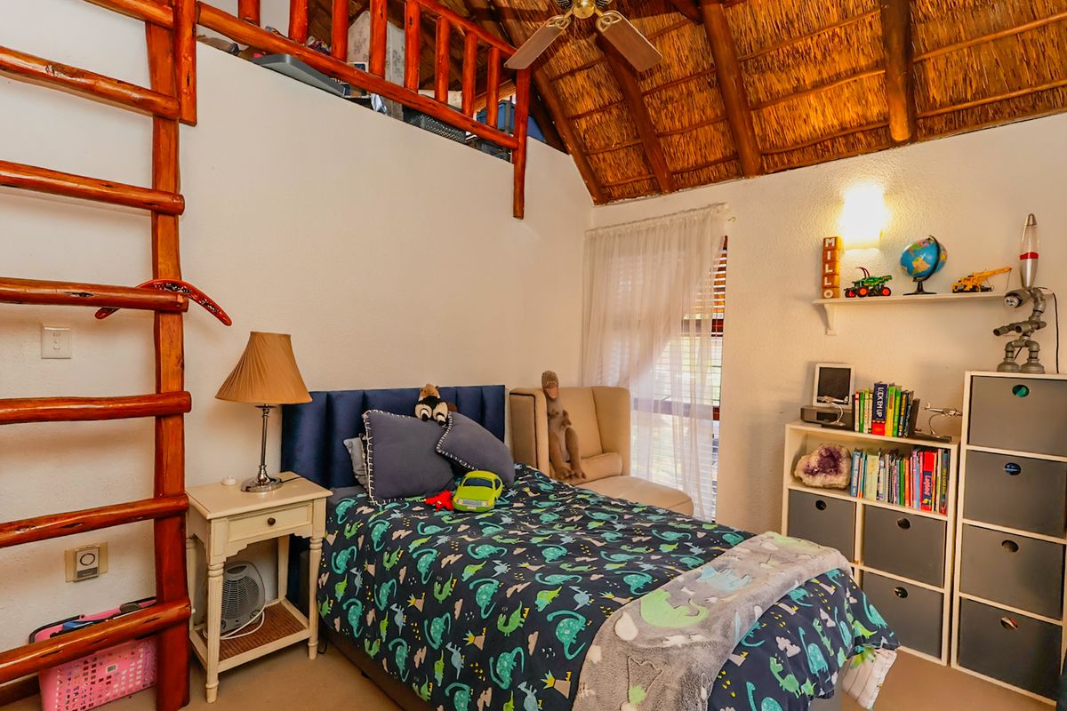 A cozy bedroom featuring a high vaulted thatched ceiling with exposed timber rafters and a built-in mezzanine loft area accessed by a wooden ladder.