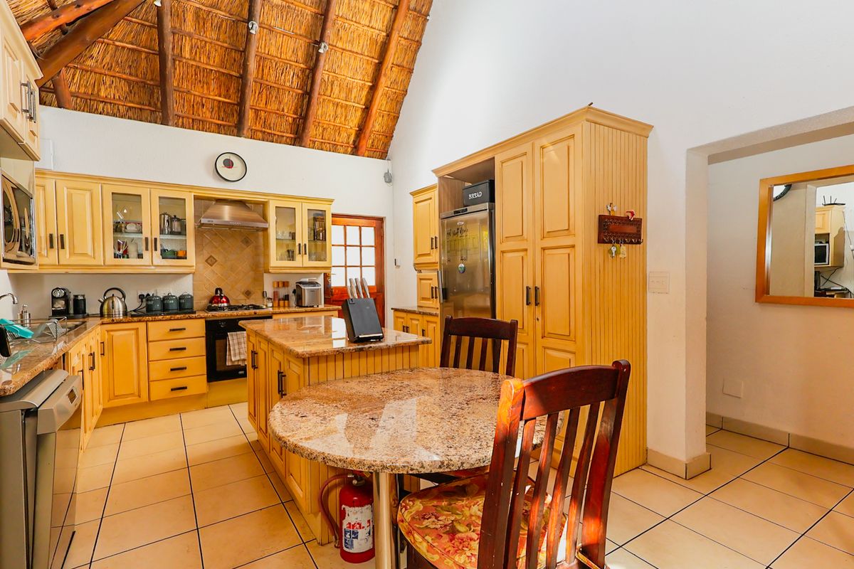 A spacious kitchen featuring a high vaulted thatch ceiling, granite countertops, a central island, and ample built-in cabinetry with tiled flooring.