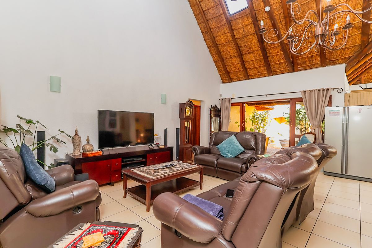 Spacious living room featuring a high vaulted thatched ceiling, exposed timber beams, a skylight, and large sliding doors opening to an outdoor area.