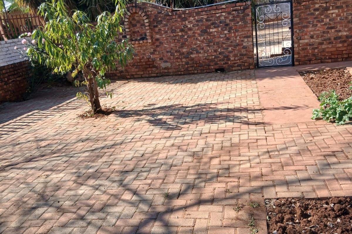 A paved rear courtyard area featuring a brick boundary wall, wrought iron gate, and established garden trees.