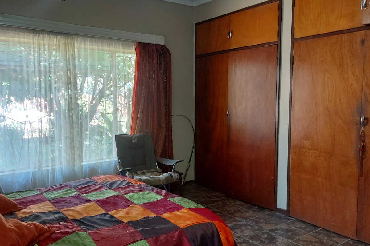 A bedroom featuring built-in wooden cupboards, tiled flooring, and a large window allowing natural light.