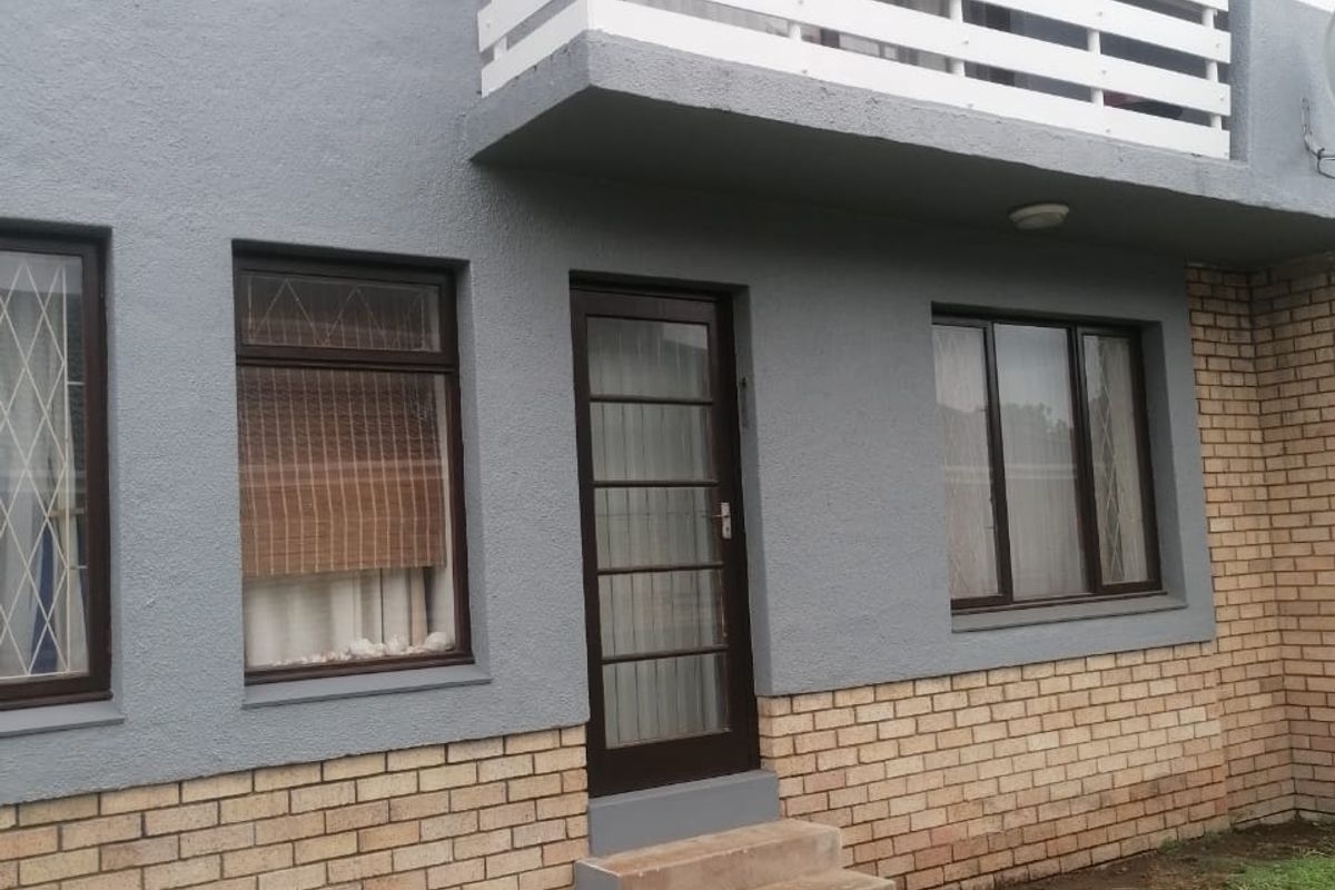 Exterior view of a townhouse featuring a brick and rendered facade, a small balcony with white railings, and a ground-level entrance with concrete steps.