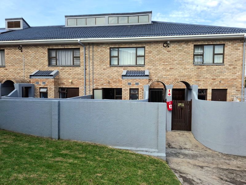 Front elevation of a face-brick townhouse featuring a tiled roof, private gated entrance, and a low-maintenance front boundary wall.