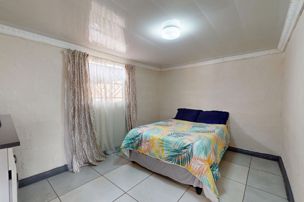 A functional bedroom featuring tiled flooring, a glossy ceiling finish, and security bars on the window.