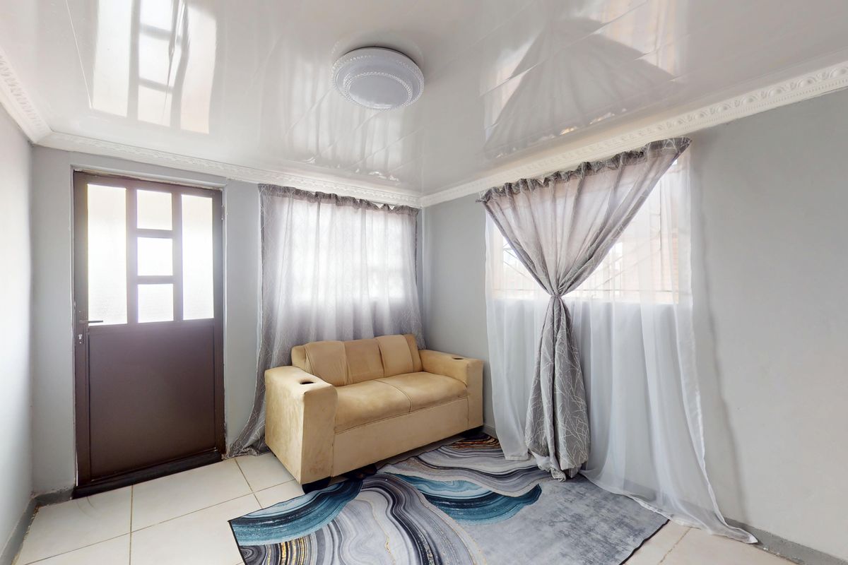 A bright living room featuring a glossy ceiling finish, tiled flooring, and a secure entrance door with natural light filtering through window curtains.