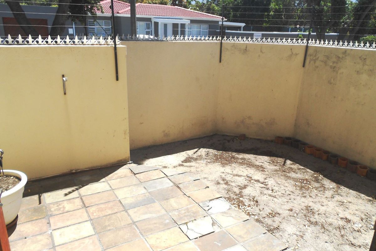A rear courtyard area featuring a small tiled patio, perimeter wall with electric fencing, and an unpaved garden section requiring maintenance.