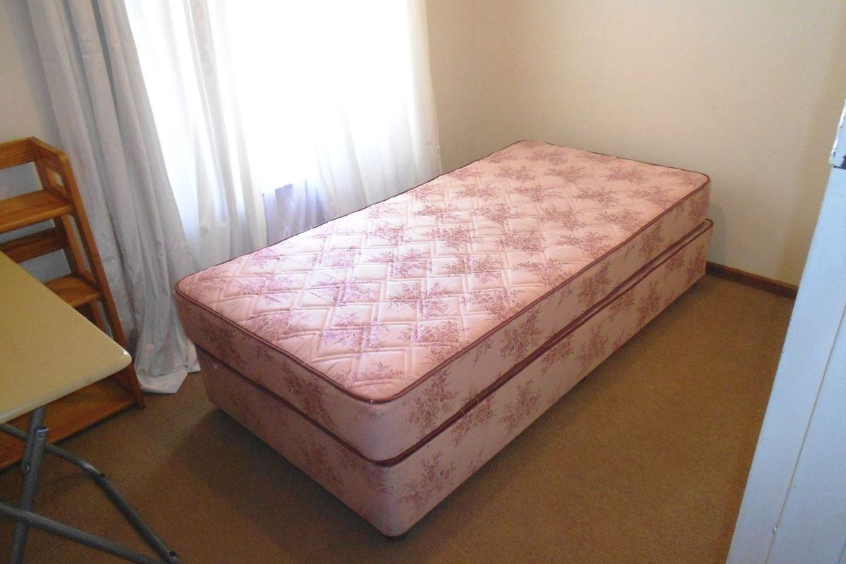 A simple bedroom featuring carpeted flooring and natural light from a window.
