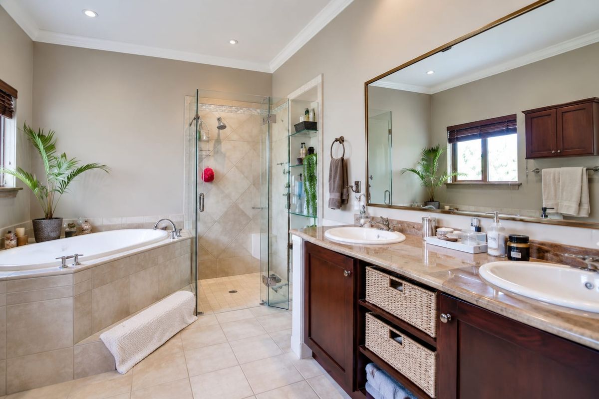 Spacious bathroom featuring a double vanity with stone countertops, a built-in bathtub, and a separate glass-enclosed shower with neutral tile finishes.