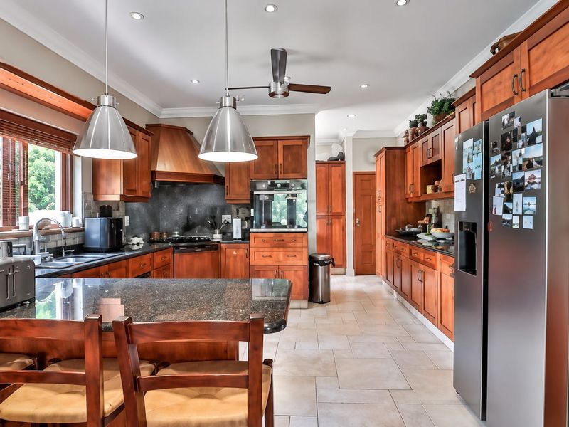Spacious kitchen featuring warm wooden cabinetry, granite countertops, built-in oven, gas hob, and tiled flooring, offering a functional and classic culinary space.