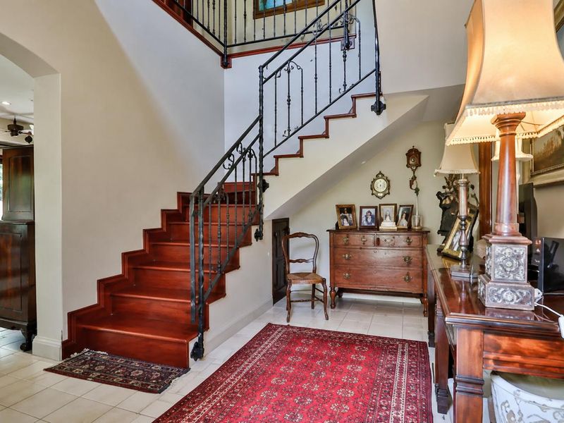 Welcoming entrance hall featuring a classic wooden staircase with decorative wrought iron balustrade and neutral tiled flooring.