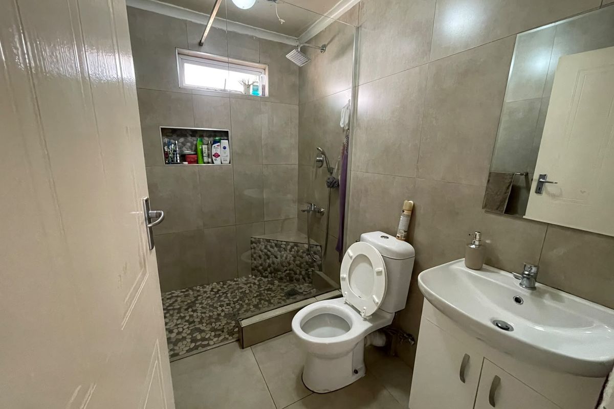 Modern bathroom featuring a walk-in shower with pebble flooring, a built-in bench, vanity cabinet, and neutral wall tiling.
