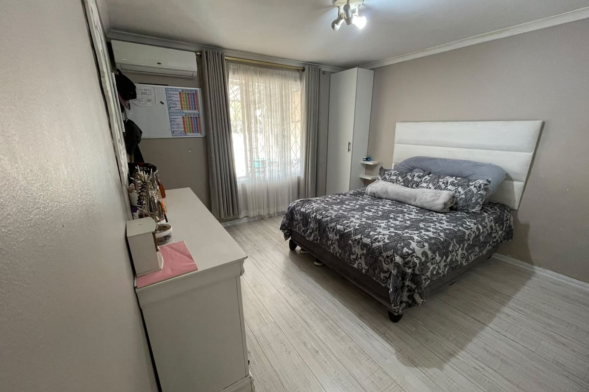 A well-maintained bedroom featuring laminate flooring, a built-in wardrobe, and a wall-mounted split-system air conditioner.