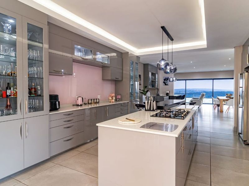 Modern open-plan kitchen featuring a central island, high-gloss cabinetry, stone countertops, and integrated appliances, flowing into a spacious living area with scenic views.