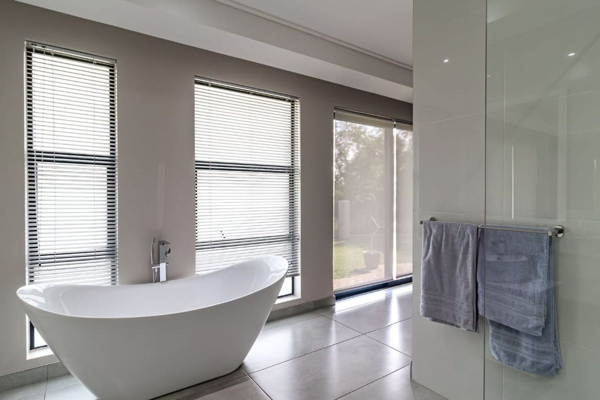 Modern bathroom featuring a sleek freestanding bathtub, large format floor tiles, and a glass-enclosed shower with natural light from multiple windows.