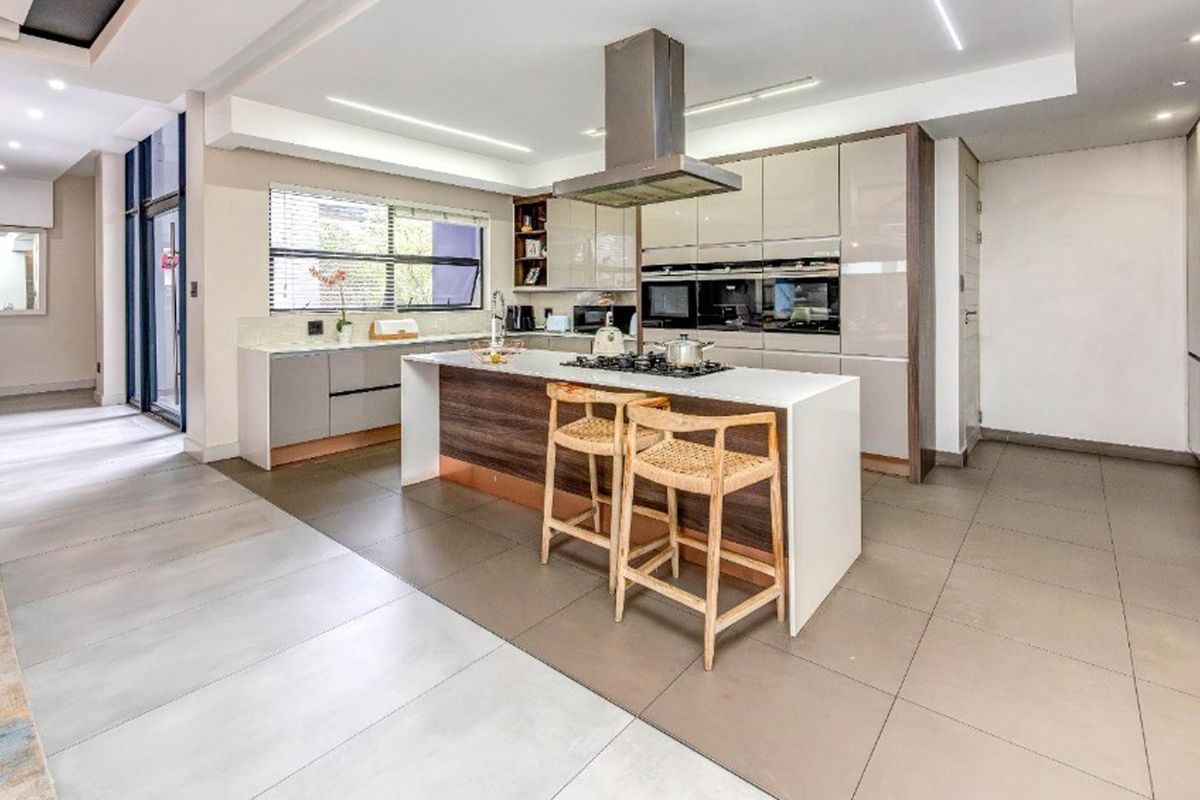 Modern kitchen featuring a central island with gas hob, built-in appliances, sleek gloss cabinetry, and large format floor tiles.