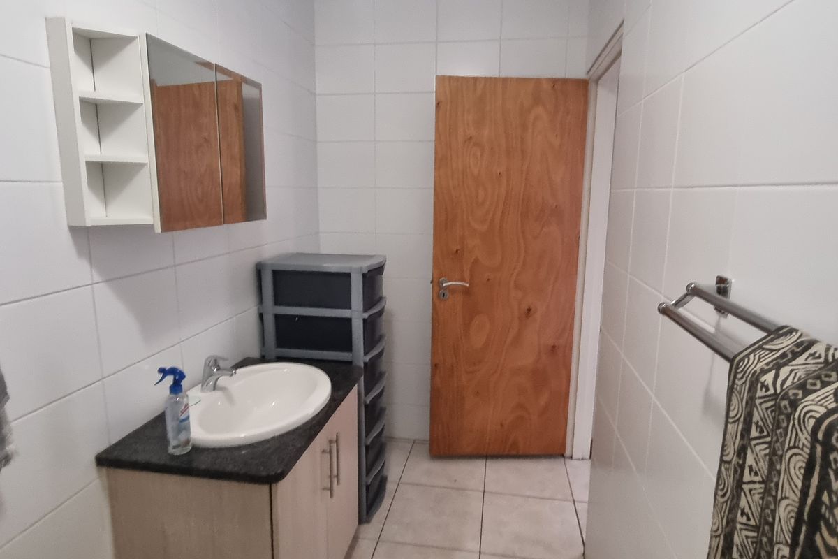 A functional bathroom featuring tiled walls and flooring, a vanity unit with a basin, and a wooden door.