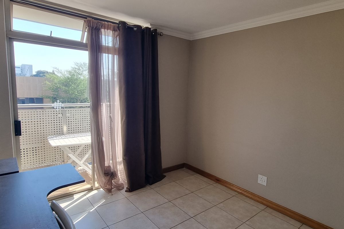 A bright, empty bedroom featuring tiled flooring, neutral walls, and a sliding glass door providing access to a private balcony.