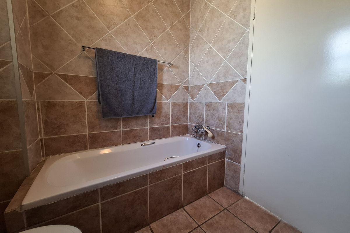 A functional bathroom featuring a built-in bathtub with tiled surround and wall cladding, offering a dated but well-maintained space.