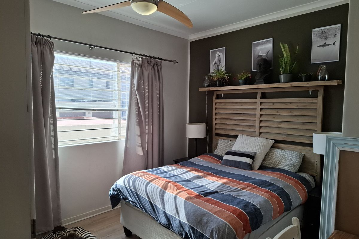 A well-maintained bedroom featuring laminate flooring, a ceiling fan, and a large window with blinds, providing a comfortable and functional living space.