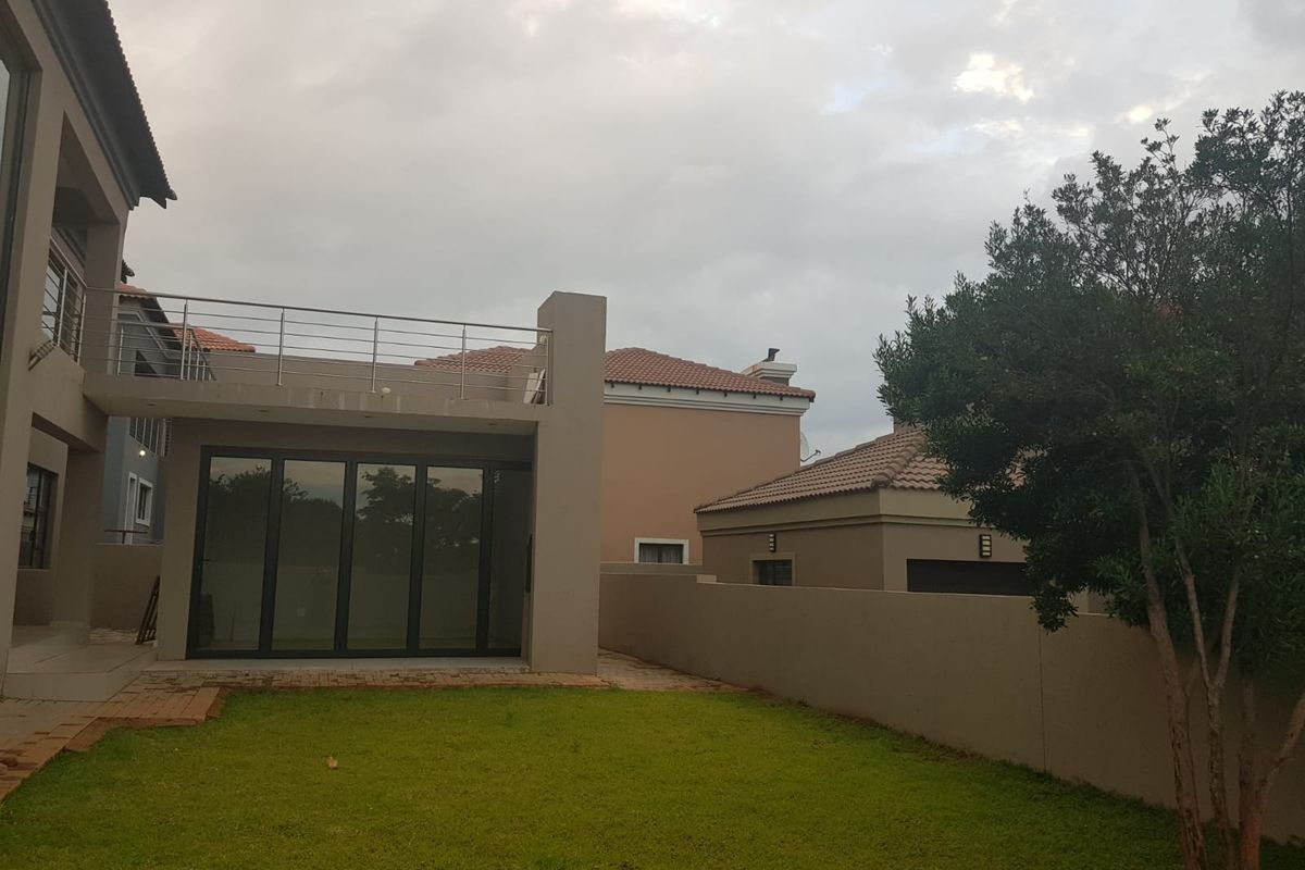Rear view of the property featuring a landscaped garden, a paved patio area, and an upper-level balcony with metal railings.