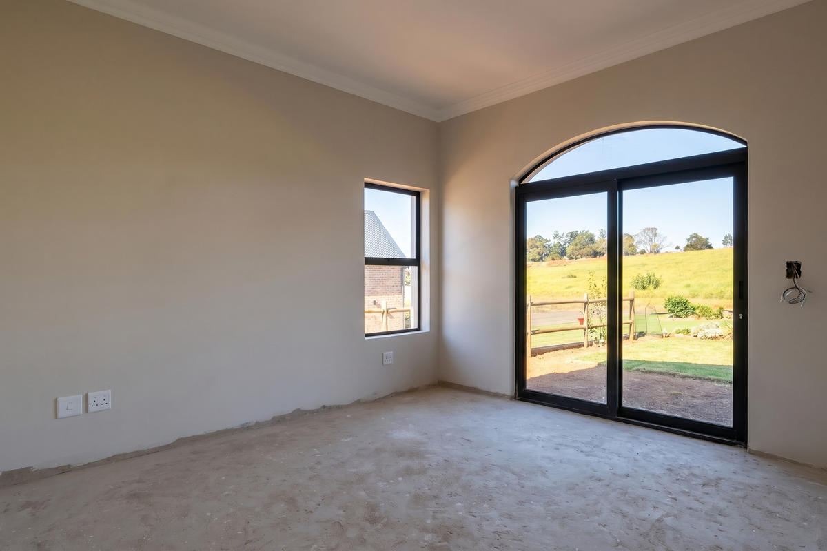 An empty, unfinished bedroom featuring a large arched sliding glass door with garden views, neutral walls, and exposed electrical wiring.