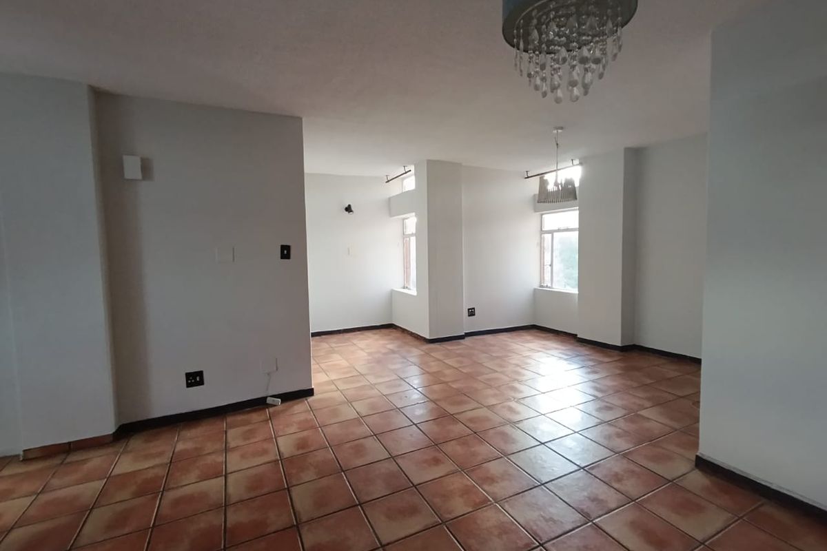 A spacious, empty living area featuring ceramic floor tiles, neutral walls, and natural light from multiple windows.
