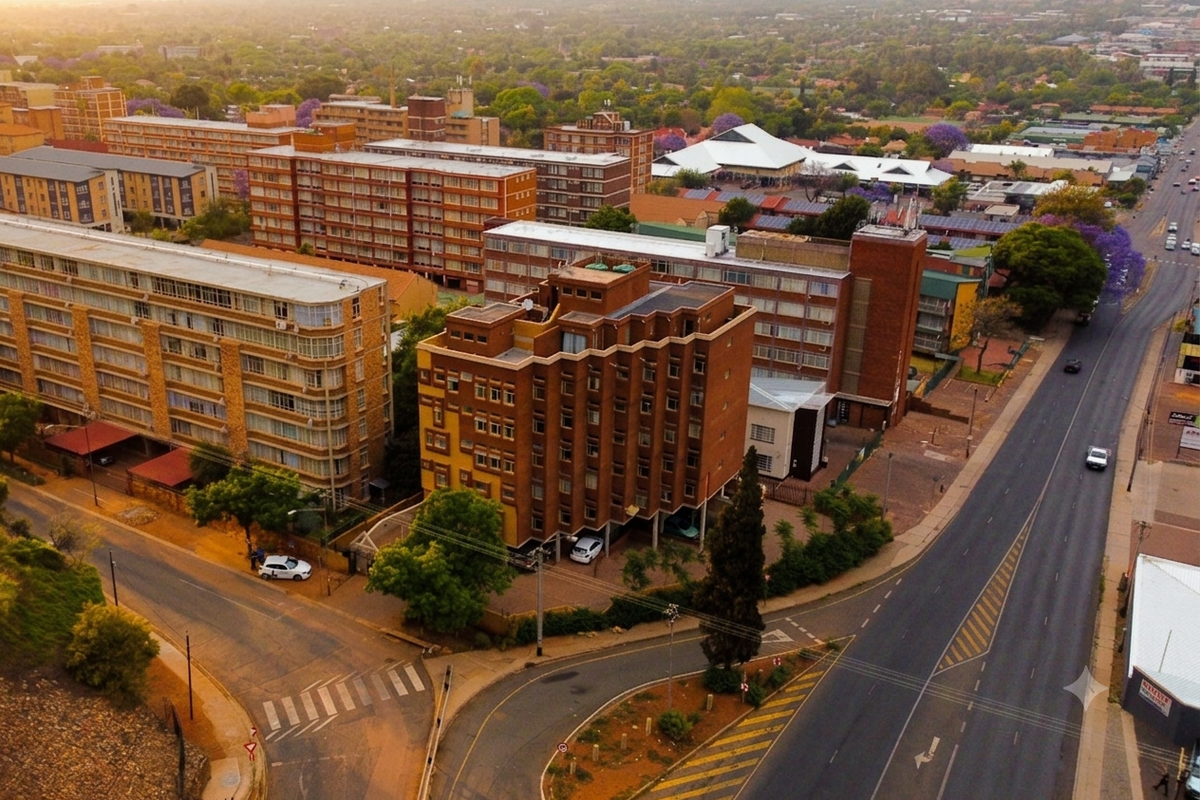An aerial view of a residential apartment complex situated in an urban neighborhood with surrounding road infrastructure and mature trees.