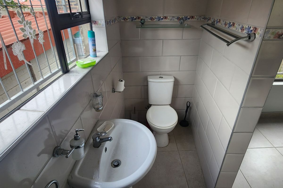 A functional bathroom featuring ceramic wall and floor tiles, a pedestal washbasin with chrome mixer, and a standard close-coupled toilet.