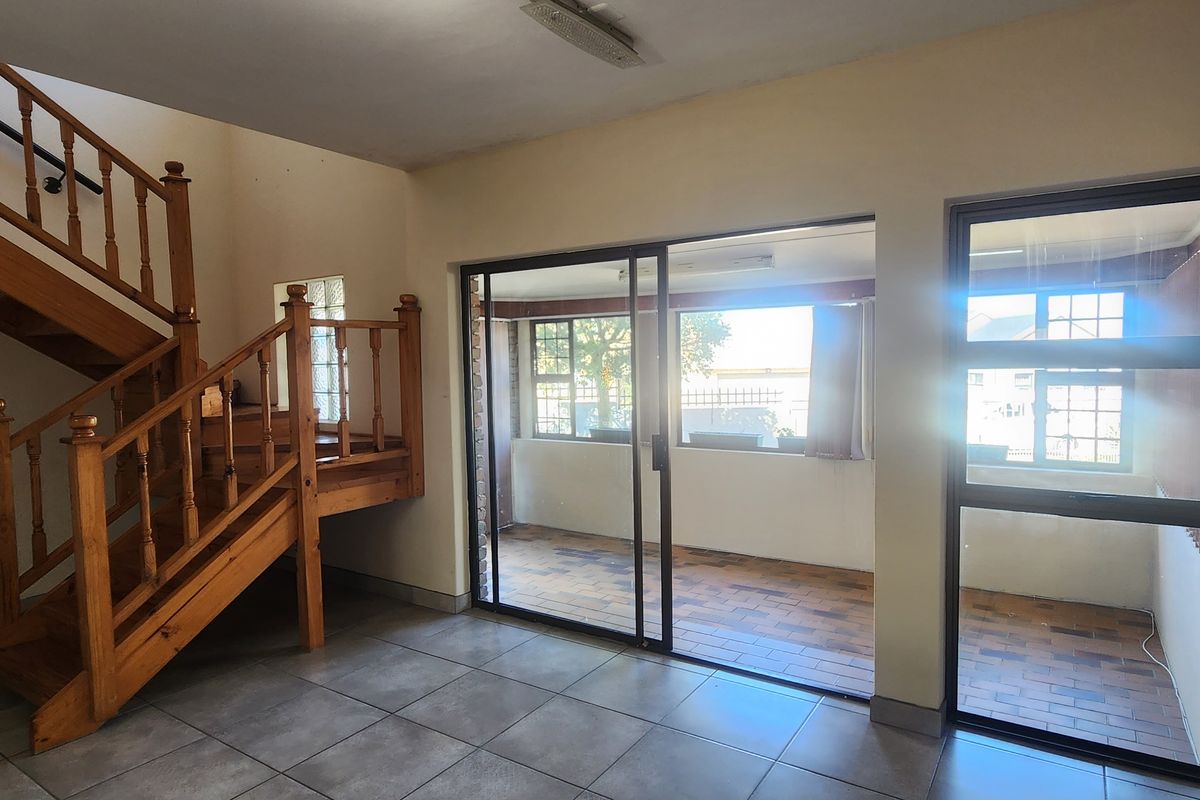 Spacious living area featuring a wooden staircase, tiled flooring, and large sliding glass doors providing access to an enclosed patio area.