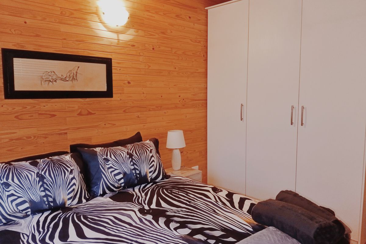 A cozy bedroom featuring warm timber wall cladding, exposed ceiling beams, and a large white built-in wardrobe for ample storage.