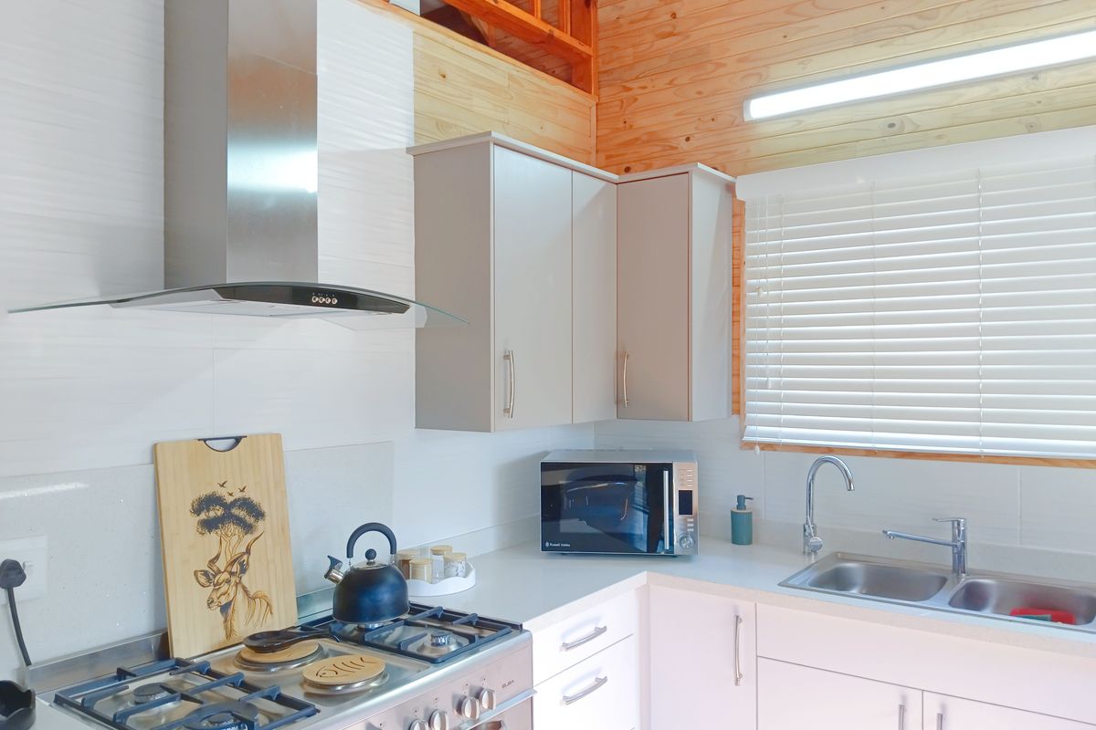 A modern kitchen featuring light-toned cabinetry, a gas stove with extractor fan, double bowl sink, and warm timber ceiling accents.