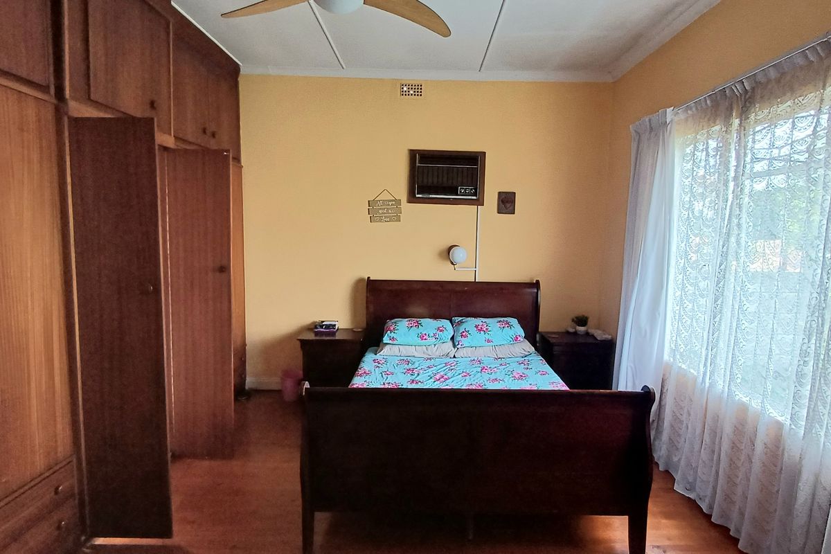 A spacious bedroom featuring extensive built-in wooden cabinetry, hardwood flooring, a ceiling fan, and a window-mounted air conditioning unit.