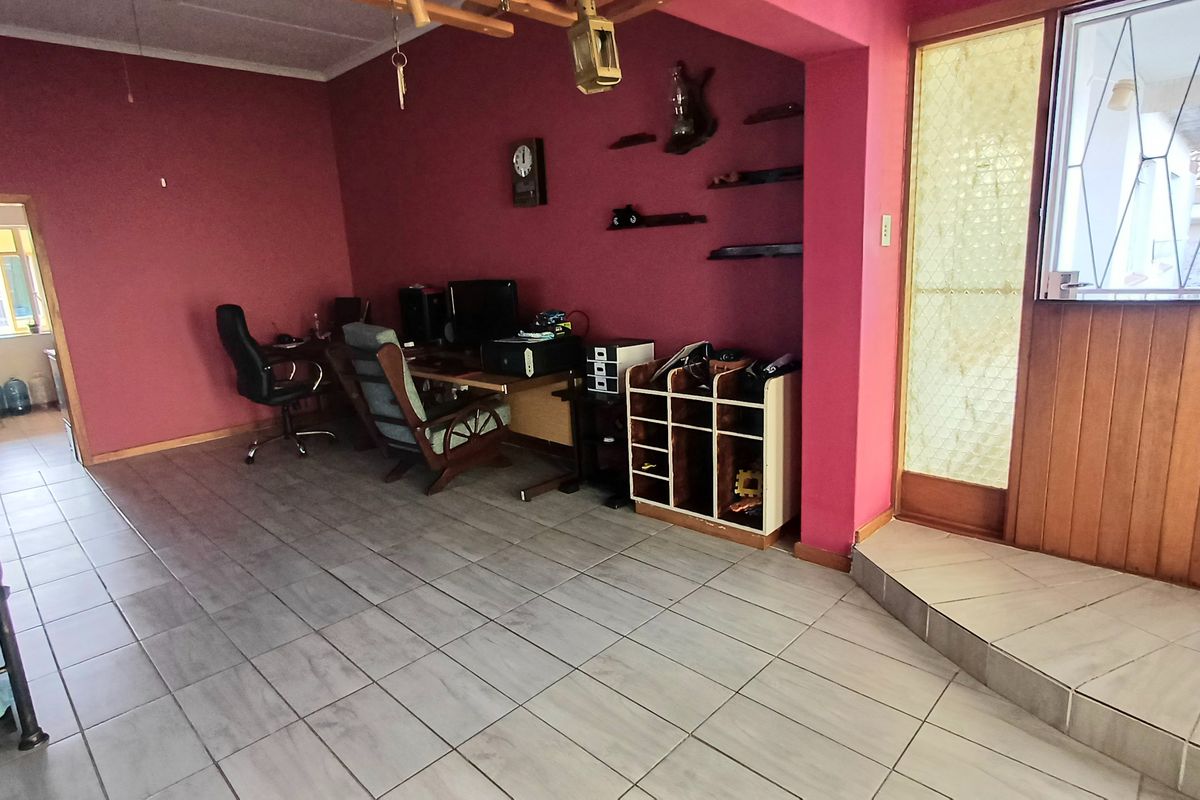 A living area featuring tiled flooring and a timber door frame with a security gate, currently utilized as a home office space.