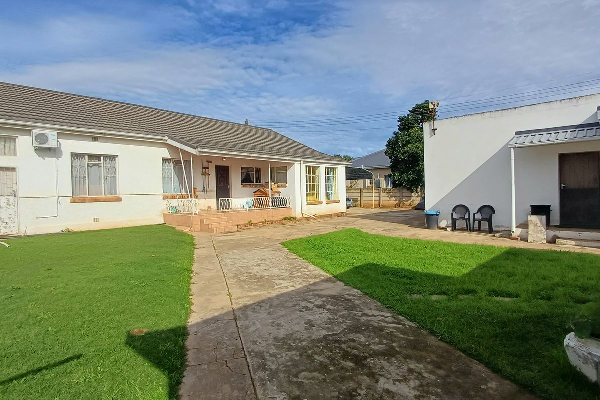 Rear view of the property featuring a concrete driveway, lawn, and covered patio area with exterior access points.