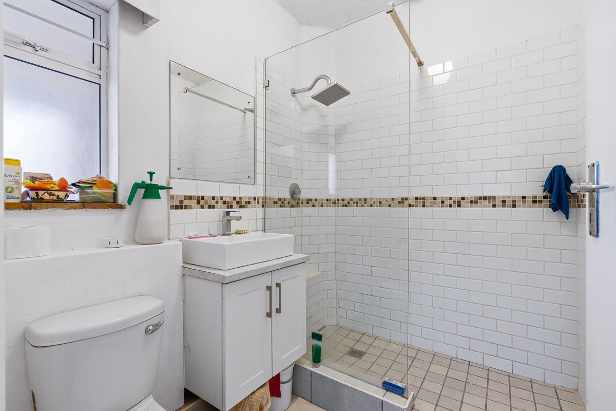 A functional bathroom featuring a walk-in shower with glass screen, vanity basin, and toilet, finished with white subway wall tiles and mosaic accents.