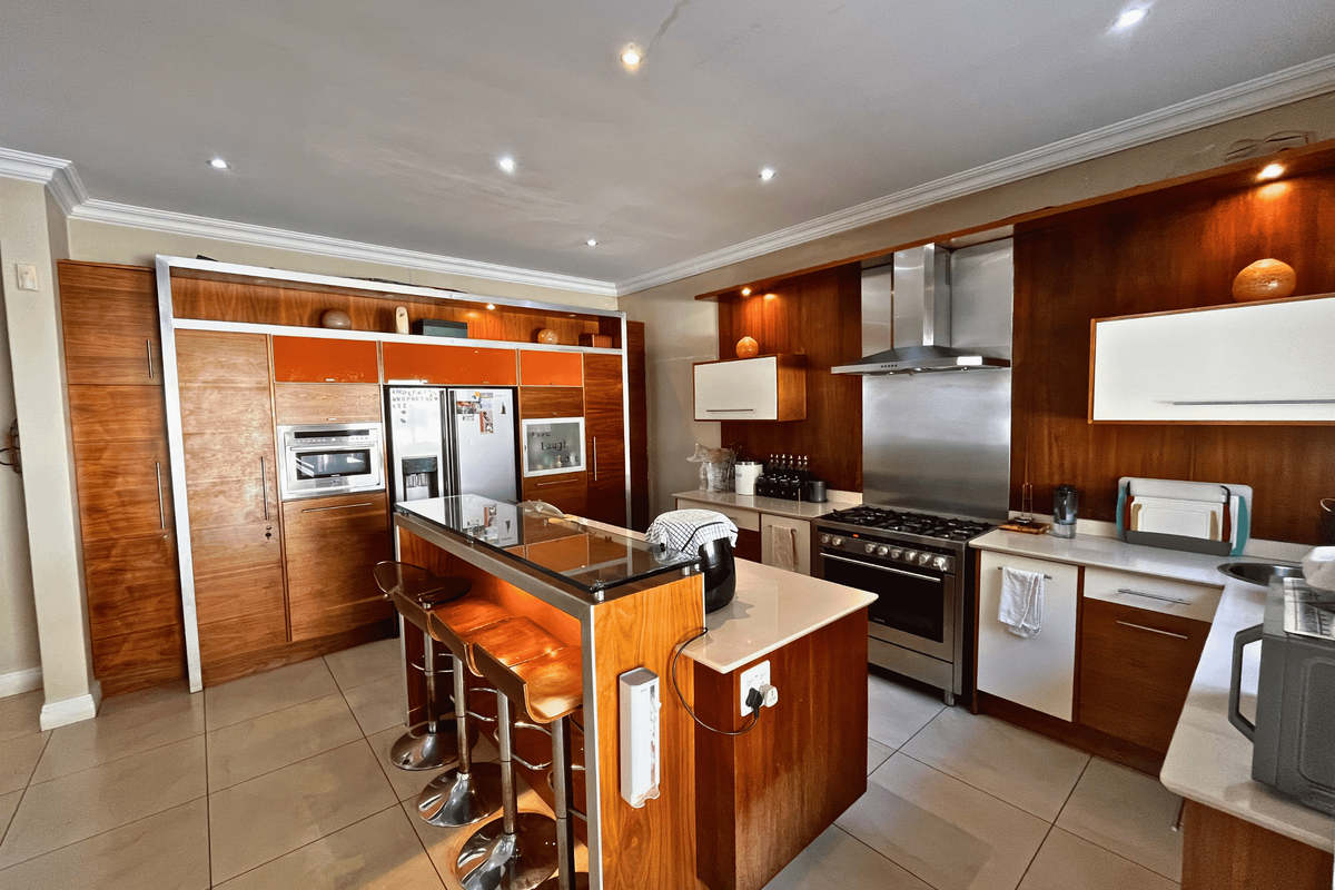 Modern kitchen featuring wood-finish cabinetry, a central island with breakfast bar, stone countertops, and integrated stainless steel appliances.