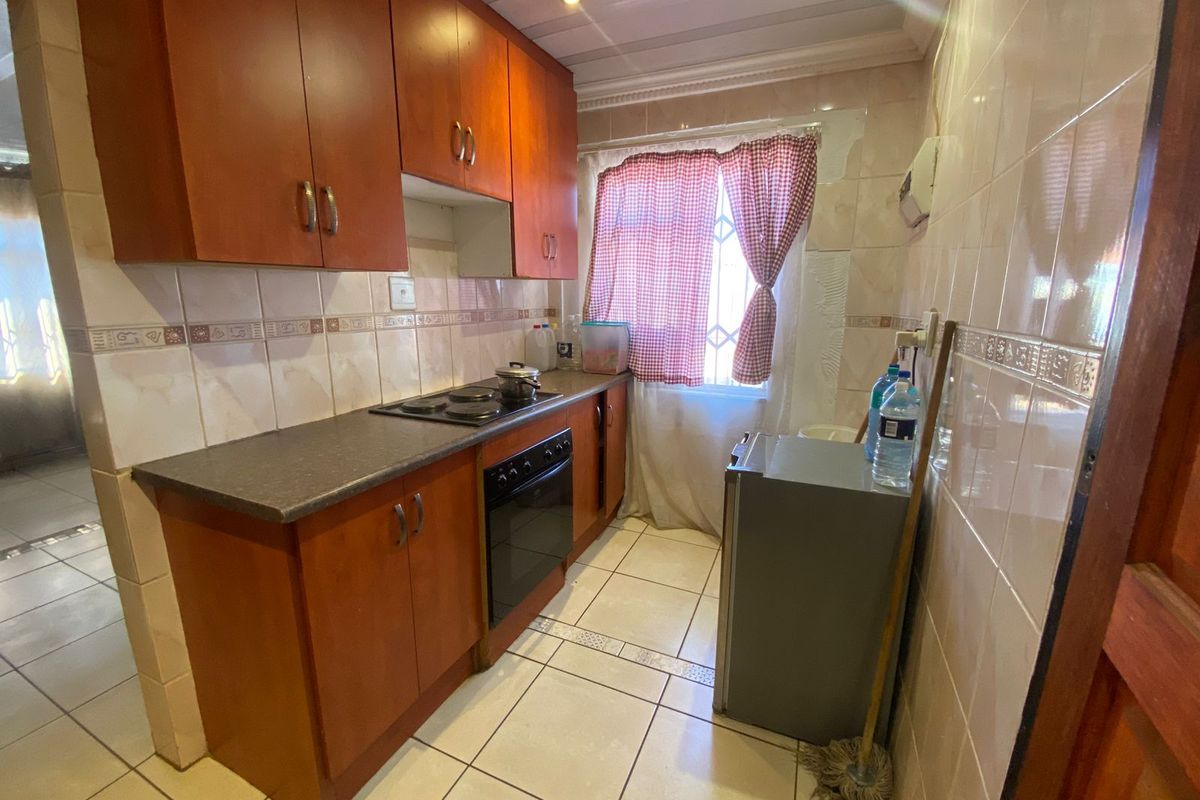 Compact kitchen featuring wooden cabinetry, built-in oven and hob, and tiled finishes. The space requires minor repairs to wall tiling and plastering.