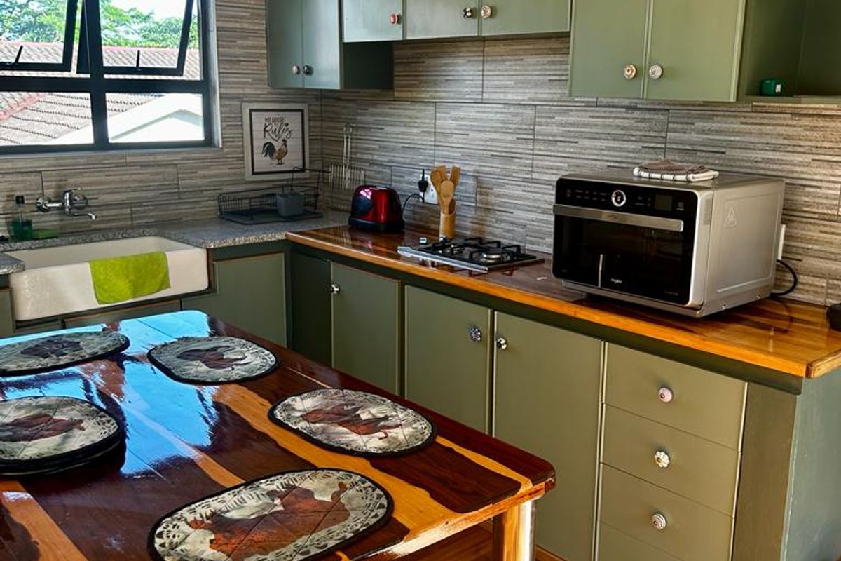 A functional kitchen featuring sage green cabinetry, wooden countertops, a farmhouse sink, and a gas hob with a modern tiled backsplash.