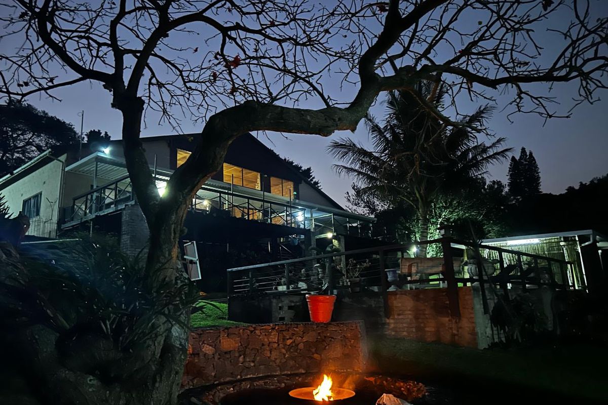 Night view of the rear exterior featuring a raised timber deck, stone retaining wall, and a built-in fire pit area.