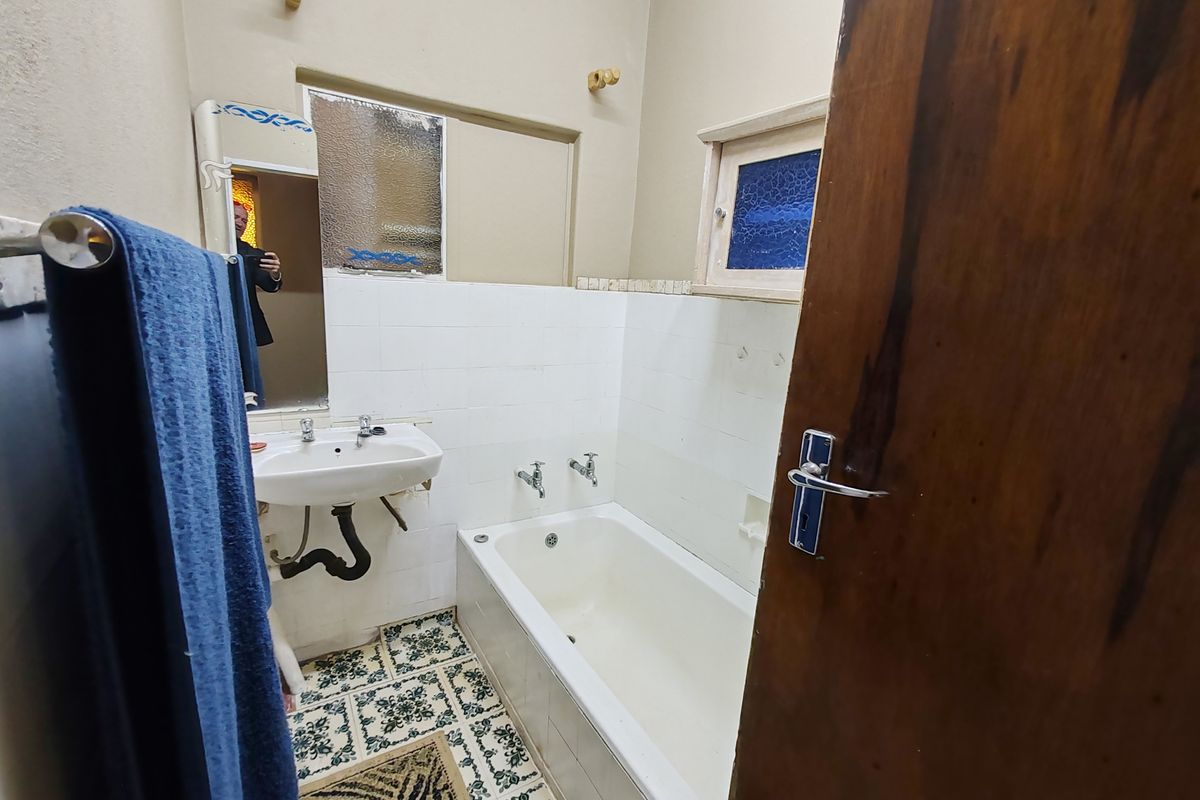 A dated bathroom featuring a pedestal basin, built-in bathtub, and patterned floor tiles, requiring cosmetic updates to modernize the space.
