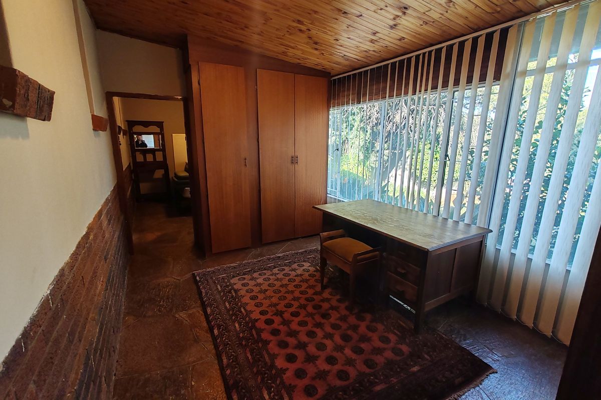 Bedroom featuring exposed brick walls, timber ceiling, stone flooring, and built-in wooden cupboards with large windows and vertical blinds.