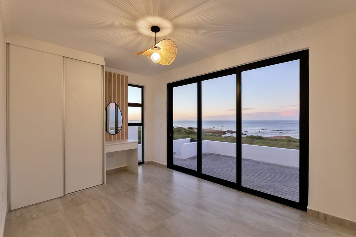 Modern bedroom featuring built-in cabinetry, a vanity area, and large sliding glass doors opening to a patio with scenic ocean views.