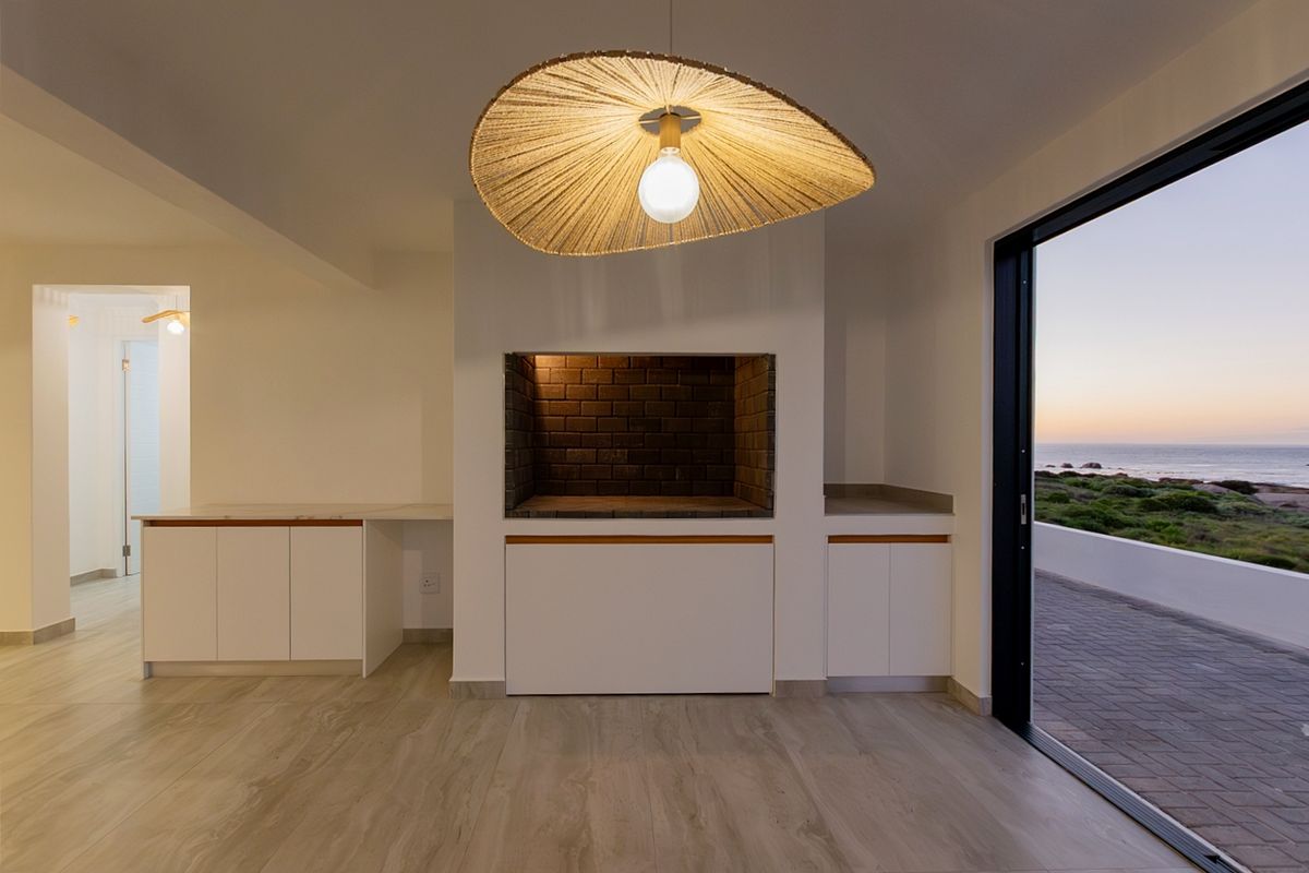 Modern living area featuring a built-in braai, sleek cabinetry, and large sliding doors opening to a scenic coastal view.